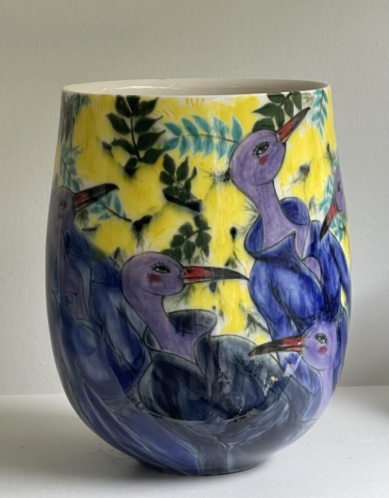 A porcelain cup with underglaze paintings of two purple flamingos with jackets and a yellow background with green leaves